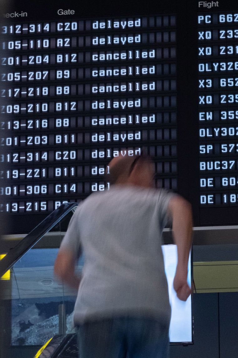 Extreme heat makes flying harder. Airlines and airports say they aren’t sweating it. 1 A person on an escalator in front of screen with delays and cancellations
