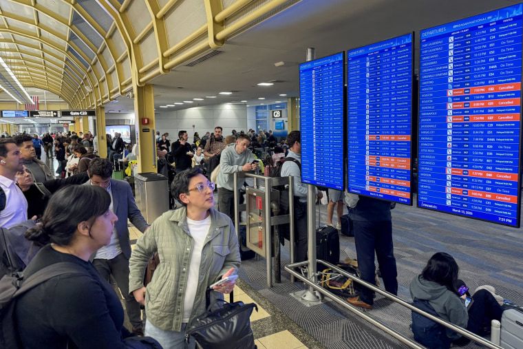 Overheated circuit board leads to ground stop at D.C. area airports 1 Travelers look at a departures screen inside a terminal.