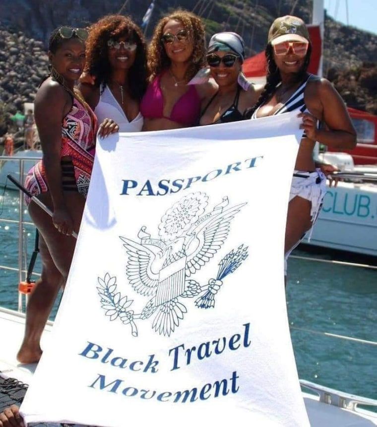 The globetrotting communities embracing Black joy through international travel 2 Travelers on a yacht posing with a Black Travel Movement towel.