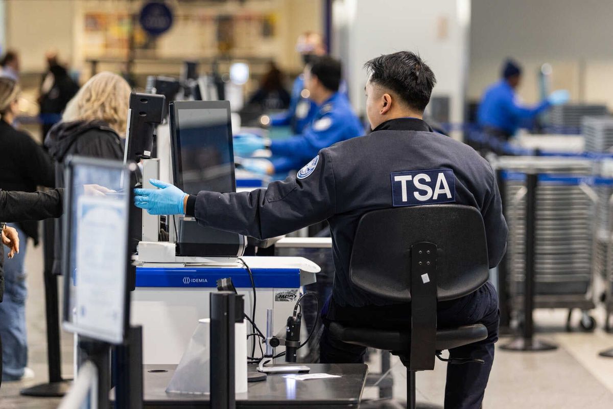 Video: Kristi Noem Hands $10,000 Bonuses to Some T.S.A. Agents 1 A person with a blue jacket that says TSA sits behind a computer.