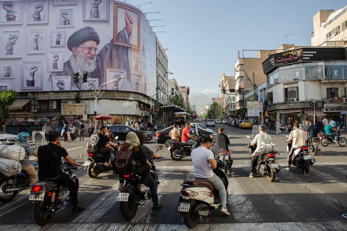 Video: Trump Says U.S. Close to Peace Agreement With Iran 1 People walk and ride scooters on a street. A building behind them has a mural of a bearded person and fists with colorful armbands.